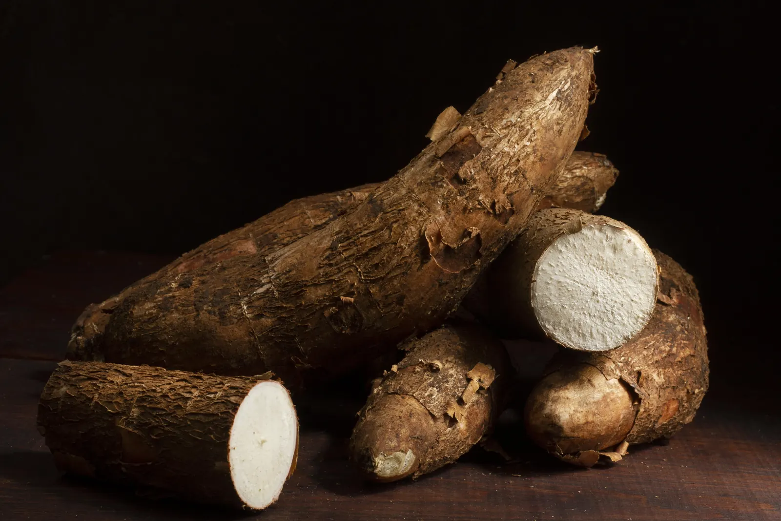 Cassava roots, one cut open, on a dark background